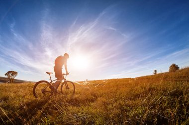 Genç bisikletçi dağ bisikletçi gündoğumu karşı kırsal alanında yol ile.