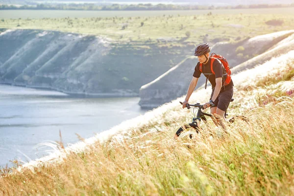 Atraktivní cyklista rirding horské kolo nad krásnou řekou v poli na venkově. — Stock fotografie