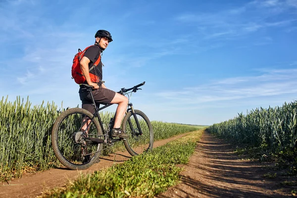 Atractivo un ciclista en bicicleta de montaña en el camino cerca de campos verdes en el campo en la temporada de verano . — Foto de Stock