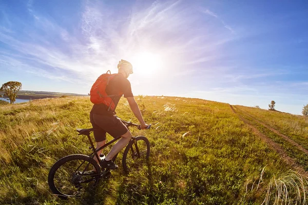 Ung cyklist med mountain cyklist på väg av fältet på landsbygden mot soluppgången. — Stockfoto
