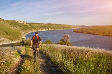 Genç adam sürme dağ bisikleti kırsal mavi nehir üzerinde yeşil çayır üzerinde.