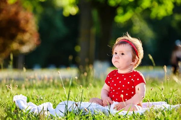 Linda adorable niña bonita en vestido de primavera rojo sonriendo sentado debajo del árbol — Foto de Stock