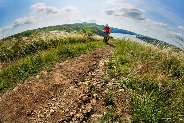 Jeune cycliste à vélo de montagne à travers prairie verte contre un ciel magnifique . — Photo