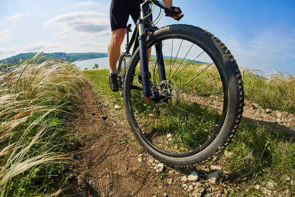 Young cyclist riding mountain bicycle through green meadow against beautiful sky.