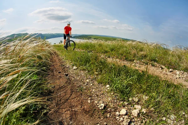 Junge Radfahrerin fährt mit Mountainbike durch grüne Wiese gegen schönen Himmel. — Stockfoto