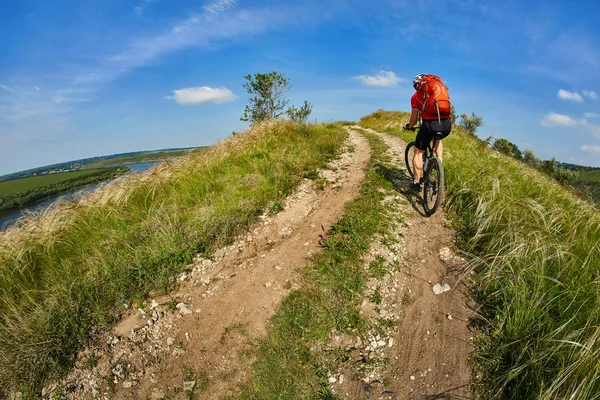 Junge Radfahrerin fährt mit Mountainbike durch grüne Wiese gegen schönen Himmel. — Stockfoto