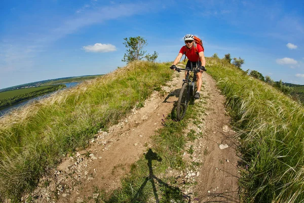 Joven ciclista montando bicicleta de montaña a través del prado verde contra el hermoso cielo . — Foto de Stock