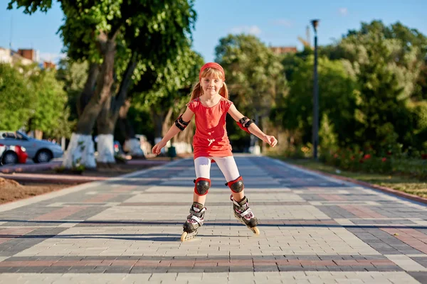 Pretty little girl in red t-shirt learning to roller skate outdoors on beautiful summer day — Stock Photo, Image
