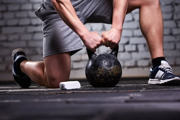 Foto da vicino del giovane sportivo mentre si accovaccia su una gamba e tiene il kettlebell contro il muro di mattoni . — Foto Stock