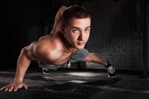 Porträt eines jungen Sportlers bei Liegestützübungen mit einer Hand gegen Ziegelwand im Fitnessstudio. — Stockfoto