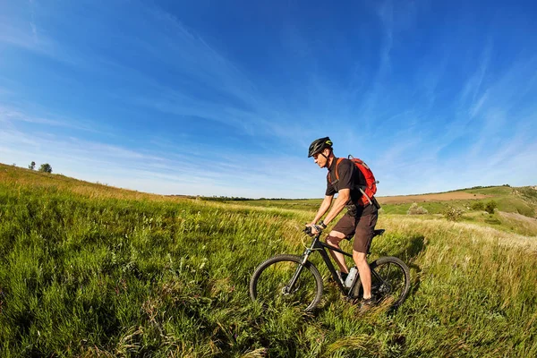 Joven montado en una bicicleta en el prado verde con una mochila —  Fotos de Stock