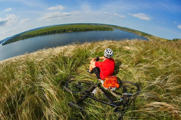Junger Radfahrer rastet mit Mountainbike gegen schönen Himmel auf der Wiese aus. — Stockfoto