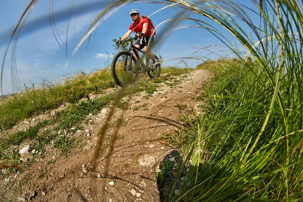 Young cyclist riding mountain bicycle through green meadow against beautiful sky.