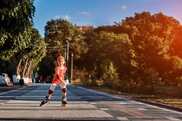 Pretty little girl in red cloth learning to roller skate outdoors on beautiful summer day in city park. — Stock Photo, Image