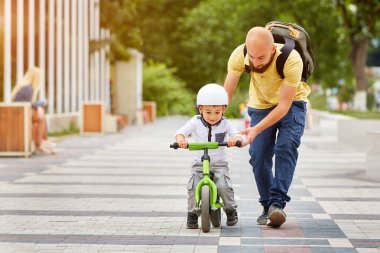 Baba oğlunun bisiklete binmesine yardım et.