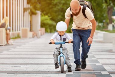 Baba oğlunun bisiklete binmesine yardım et.