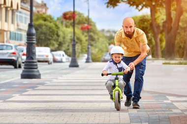Baba oğlunun bisiklete binmesine yardım et.