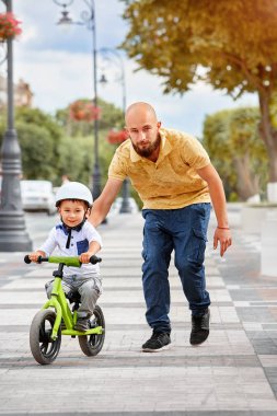 Baba oğlunun bisiklete binmesine yardım et.