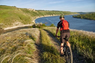 Bisikletçi dağ bisikleti üzerinde sırt çantası ile seyahat waterside üzerinde. Gezgin adventur çayır on riverside üzerinde vardır.