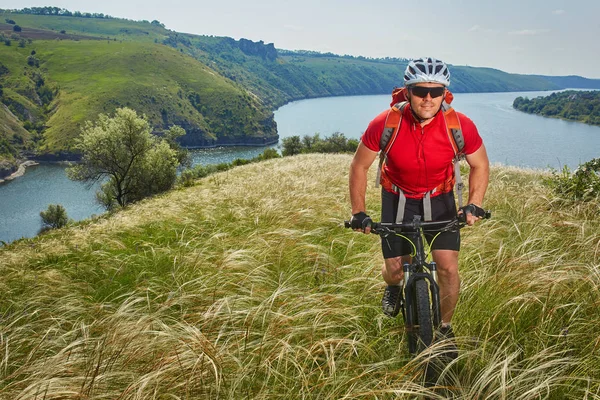 Cyklista má dobrodružství na horském kole přes zelenou louku proti krásné nebe. — Stock fotografie