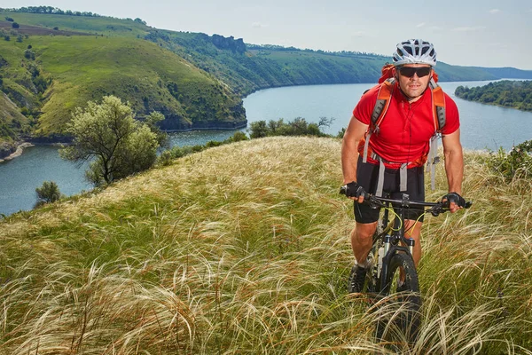 Cyklista má dobrodružství na horském kole přes zelenou louku proti krásné nebe. — Stock fotografie