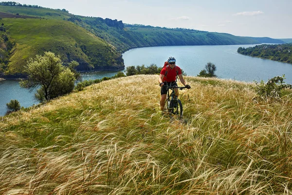 Mladý cyklista jízdní horské kolo přes zelenou louku proti krásné nebe. — Stock fotografie