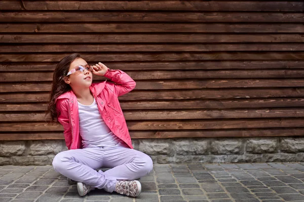 Eleganta lilla flicka barnet bär en sommar eller höst rosa jacka, vita jeans, solglasögon — Stockfoto