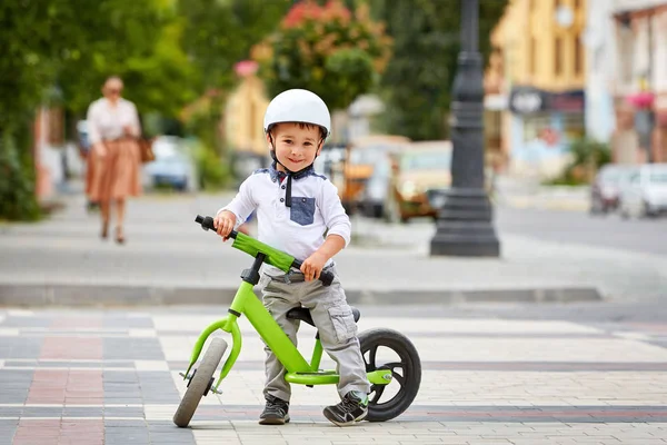 Счастливый мальчик в белом шлеме едет на своем первом велосипеде — стоковое фото