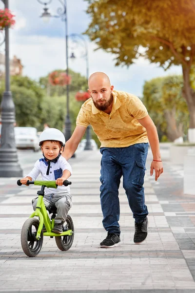 Baba oğlunun bisiklete binmesine yardım et.