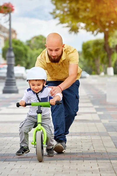 Baba oğlunun bisiklete binmesine yardım et.