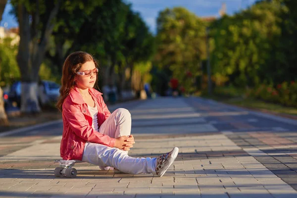 Menina vestindo capacete sentado em um skate em belo parque de verão — Fotografia de Stock