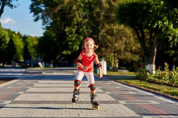 Ragazza a cavallo su pattini a rotelle in skatepark estate all'aperto. Bambino in tuta rossa per i rulli — Foto Stock