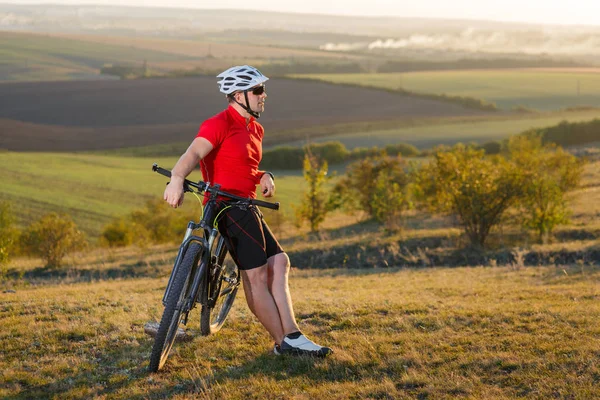 Motoros utazási mountain bike. Őszi táj. Sportoló kerékpár piros jersey és fehér sisak — Stock Fotó