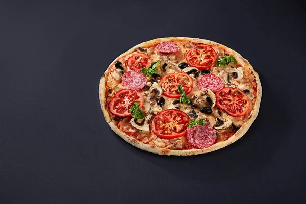 Ingredientes alimentarios y especias para cocinar y deliciosa pizza italiana sobre fondo de hormigón negro . — Foto de Stock