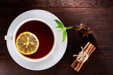 Beyaz porselen fincan çay tarçın, limon, nane yaprakları ve ahşap rustik tabloda çay süzgeci.