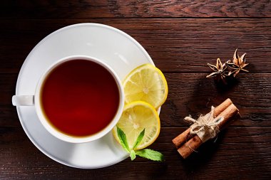 Beyaz porselen fincan çay tarçın, limon, nane yaprakları ve ahşap rustik tabloda çay süzgeci.