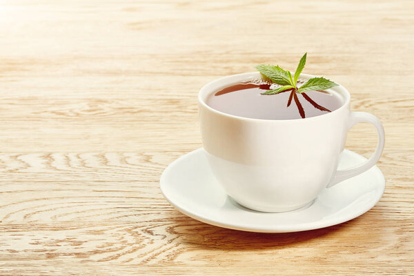 Чашка мятного чая и зеленых листьев на светлом столе
