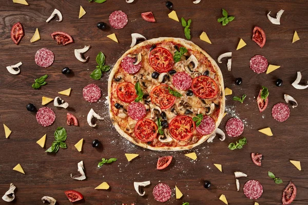 Pizza con tomates, queso mozzarella, aceitunas negras y albahaca. Deliciosa pizza italiana en tablero de pizza de madera . — Foto de Stock