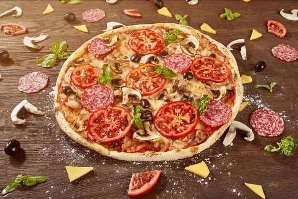Pizza con tomates, queso mozzarella, aceitunas negras y albahaca. Deliciosa pizza italiana en tablero de pizza de madera . — Foto de Stock