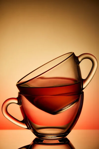Två koppar med tefat av glas. Te hälls i den översta Cup. Helium-filter ger ett vackert ljus. — Stockfoto