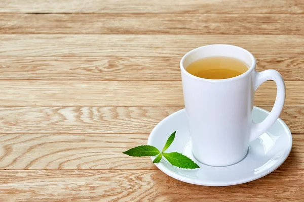 Чай с лимоном в белой чашке, коричные палочки, вязаный шерстяной шарф на деревянном столе — стоковое фото