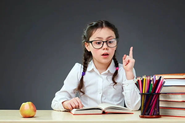 Cute industrious child is sitting at a desk indoors. Kid is learning in class on background of blackboard. — Stock Photo, Image