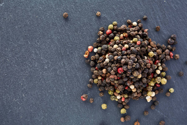 bulk of various pepper peppercorns seeds mix on dark stone