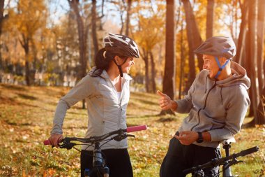 Mutlu genç çift parkta güneşli sonbahar günde bir bisiklet sürme eğleniyor. Belgili tanımlık backlight yakaladı.