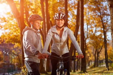 Mutlu genç çift parkta güneşli sonbahar günde bir bisiklet sürme eğleniyor. Belgili tanımlık backlight yakaladı.