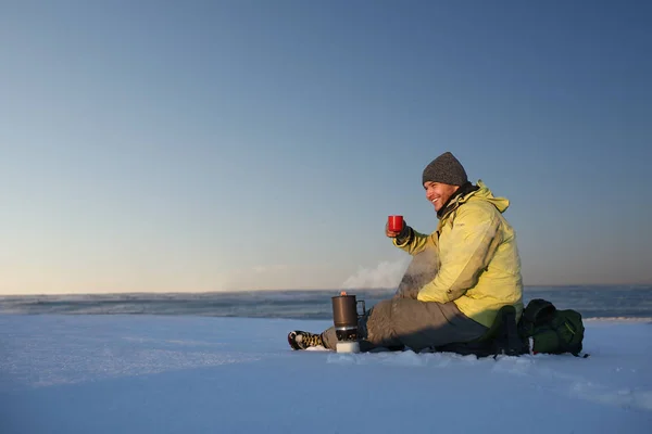 Young man drinks tea, sitting on the snow. People and healthy lifestyle concept