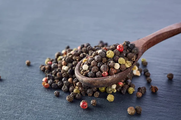 Guisantes de pimienta negra en una cuchara sobre un fondo de piedra —  Fotos de Stock