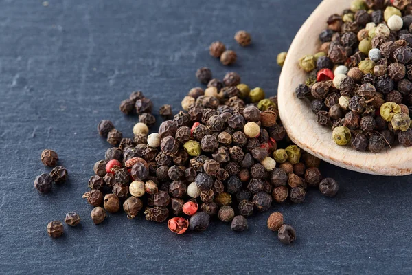 Zwarte peper erwten in een lepel op een stenen achtergrond — Stockfoto