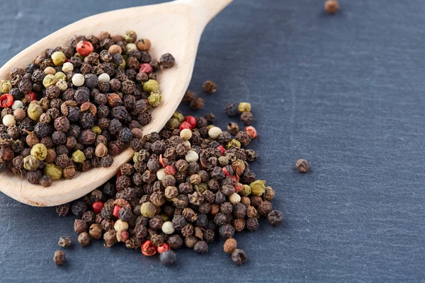 Zwarte peper erwten in een lepel op een stenen achtergrond — Stockfoto