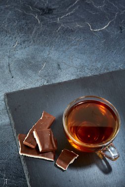 Bir cam bardak siyah çay koyu grimsi mermer zemin üzerine çikolata parçaları ile dikey resim. Üstten Görünüm